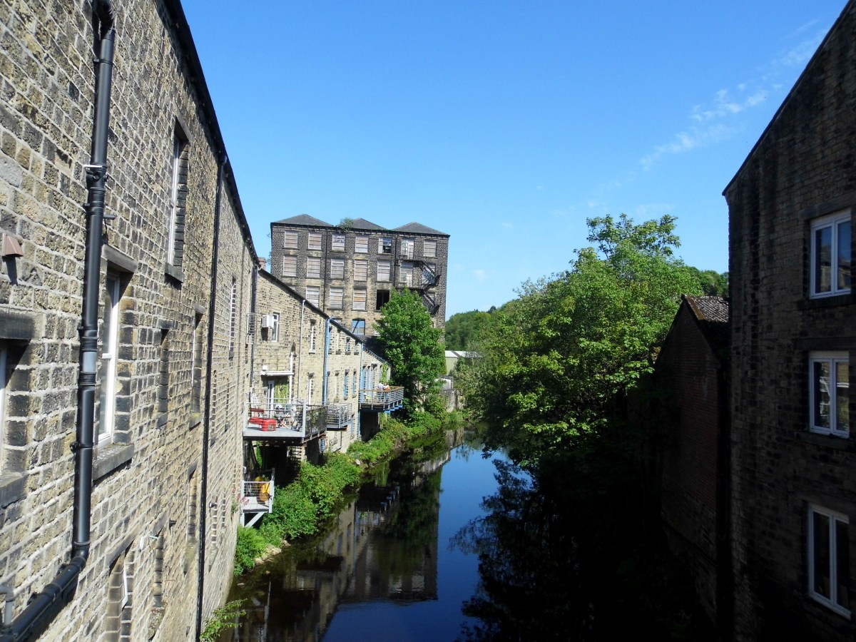 A river running through a small town on a bright sunny day, with stone buildings with balconies right next to the river and reflected in the water